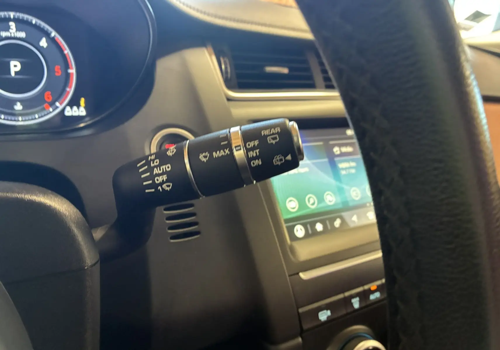 Gros plan sur la commande d’essuie-glace à gauche du volant dans l’habitacle brun et noir du Jaguar E-PACE blanc.