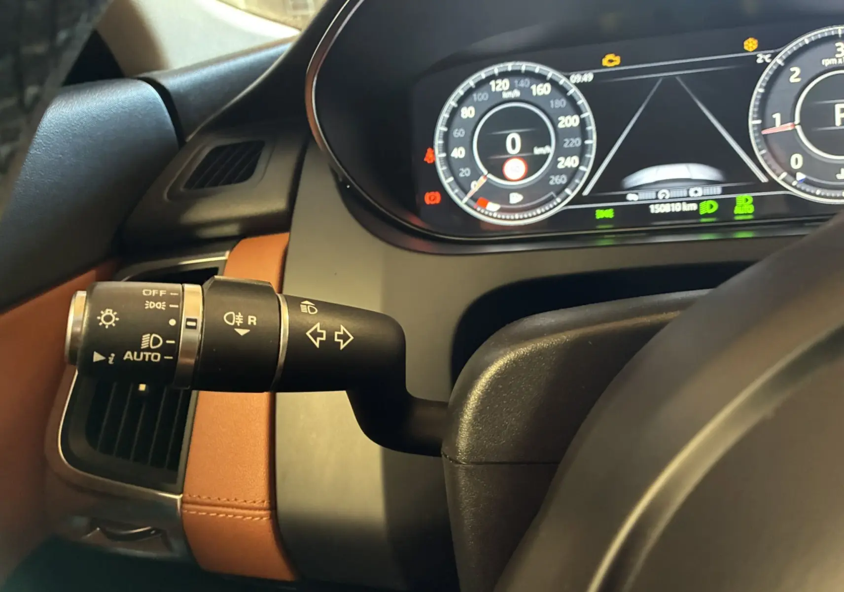 Vue intérieure rapprochée du commodo d’éclairage et du tableau de bord digital d’un Jaguar E-PACE 2019 avec sellerie cuir brun.