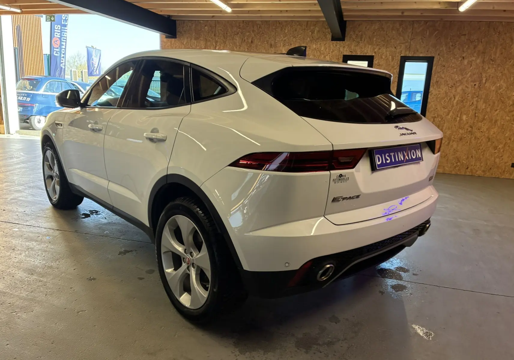 Jaguar E-PACE blanc vue 3/4 arrière droit dans un garage avec feux arrière allongés et jantes argentées.