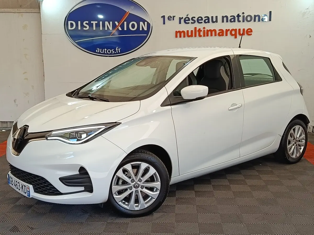 Renault ZOE Zen R135 blanc vue 3/4 avant droit, avec phares LED et jantes alliage en intérieur showroom.