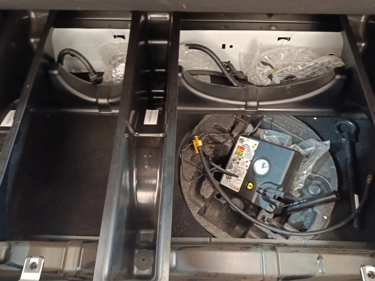 Compartiment de rangement sous le plancher du coffre de la Renault ZOE blanche, avec kit de gonflage visible.