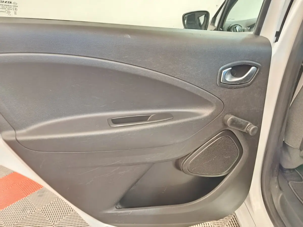 Vue intérieure de la porte arrière droite noire de la Renault ZOE Zen R135 blanche de 2021, avec poignée et manivelle de vitre.
