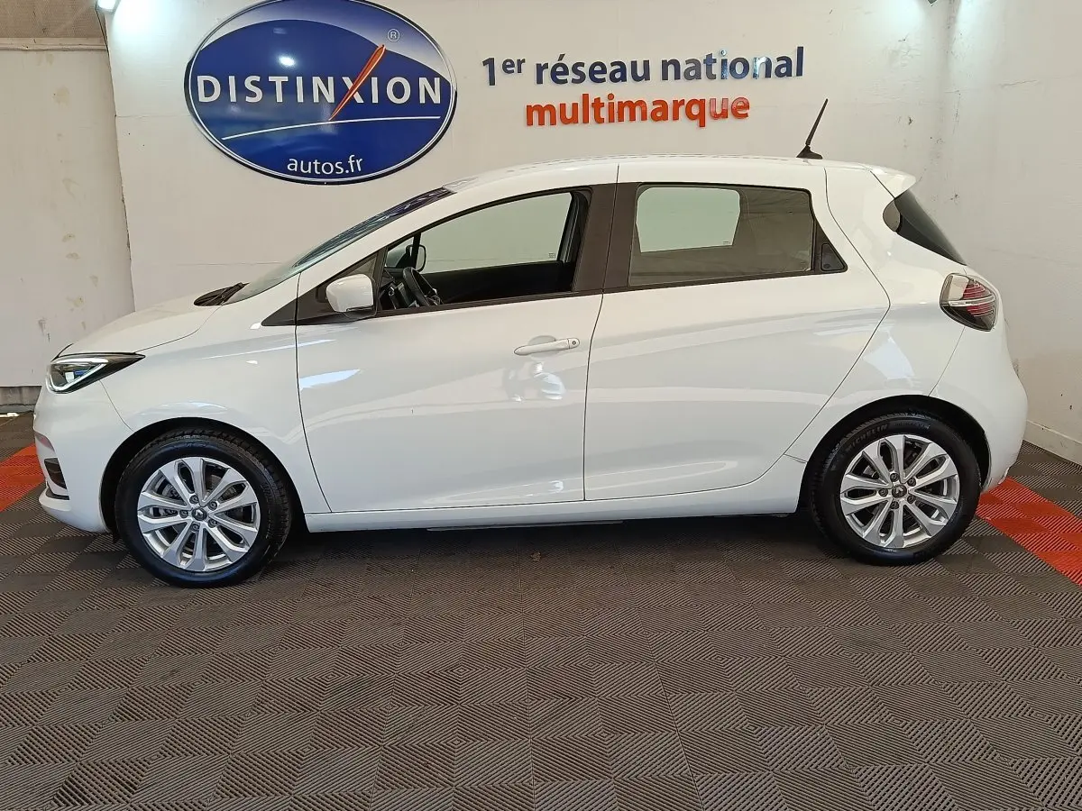 Profil côté gauche d'une Renault ZOE blanche 2021 Zen R135 électrique, avec jantes alliage et vitres teintées.