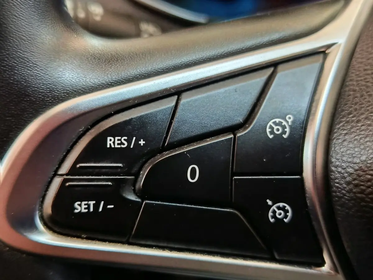 Gros plan sur les commandes du régulateur de vitesse au volant cuir synthétique d'une Renault ZOE blanche.