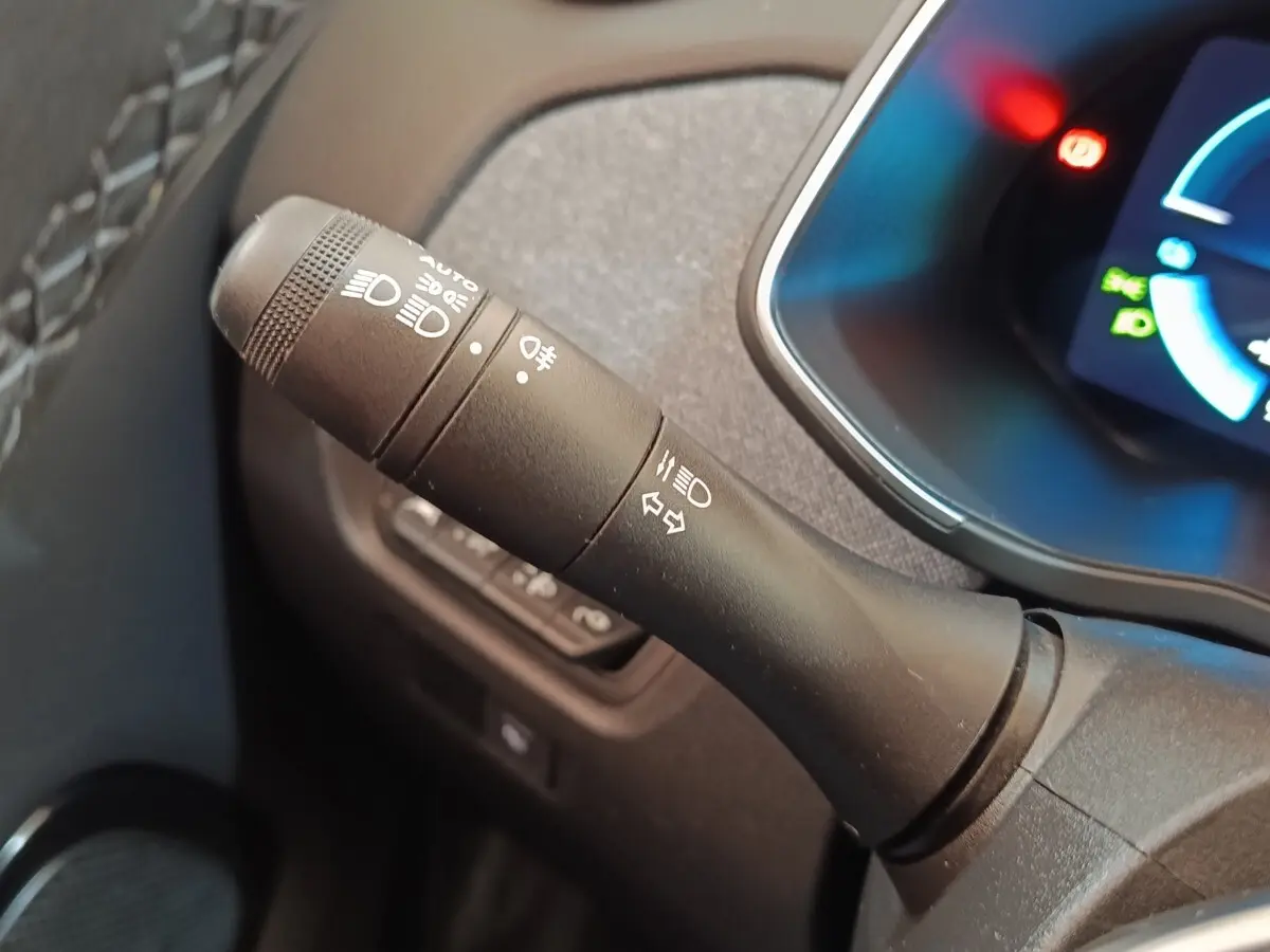 Gros plan sur la manette de commandes des phares et clignotants dans l'habitacle noir du Renault ZOE blanc 2021.