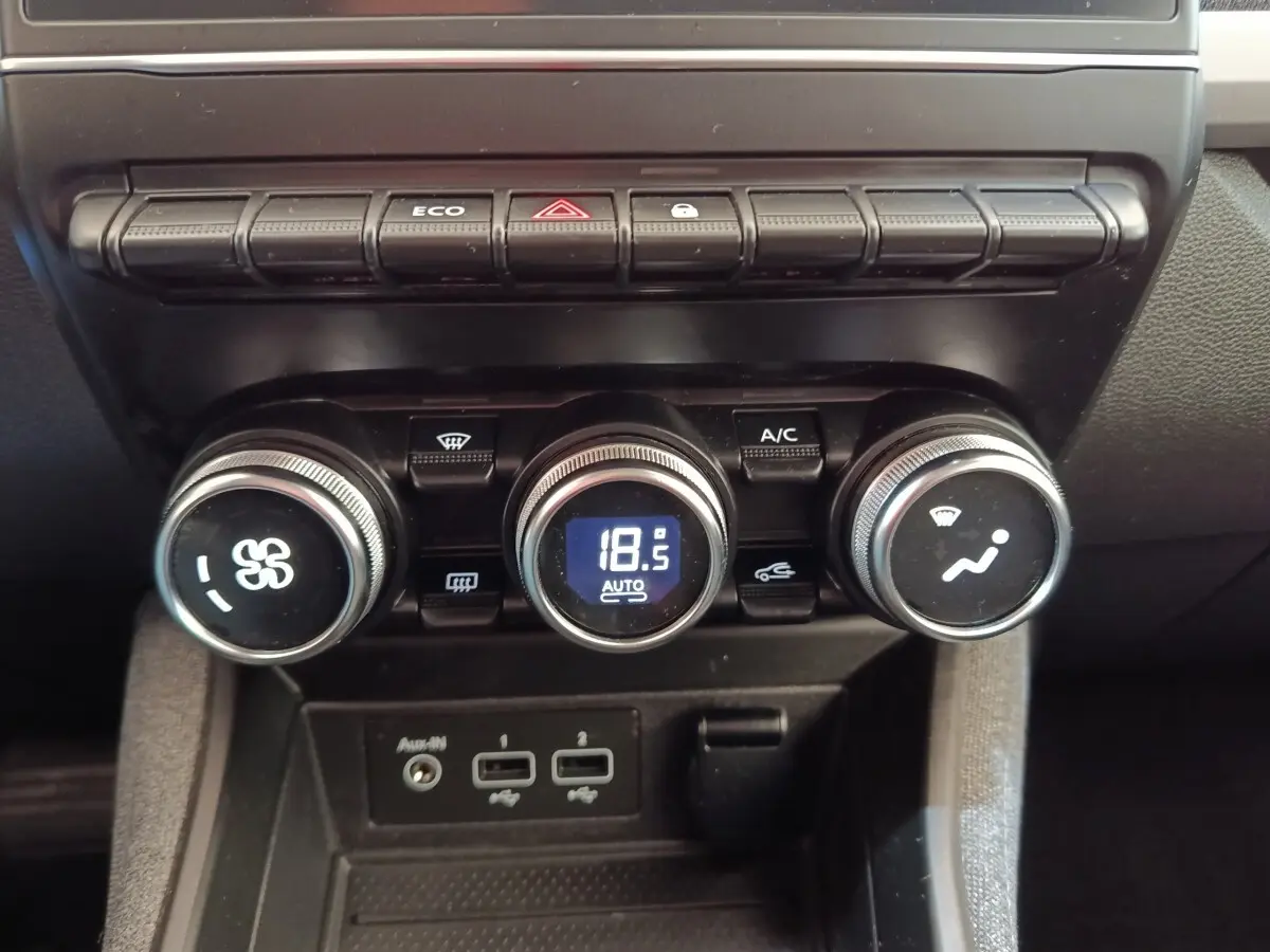 Gros plan sur la console centrale de la Renault ZOE blanche, montrant les commandes de climatisation et les ports USB.