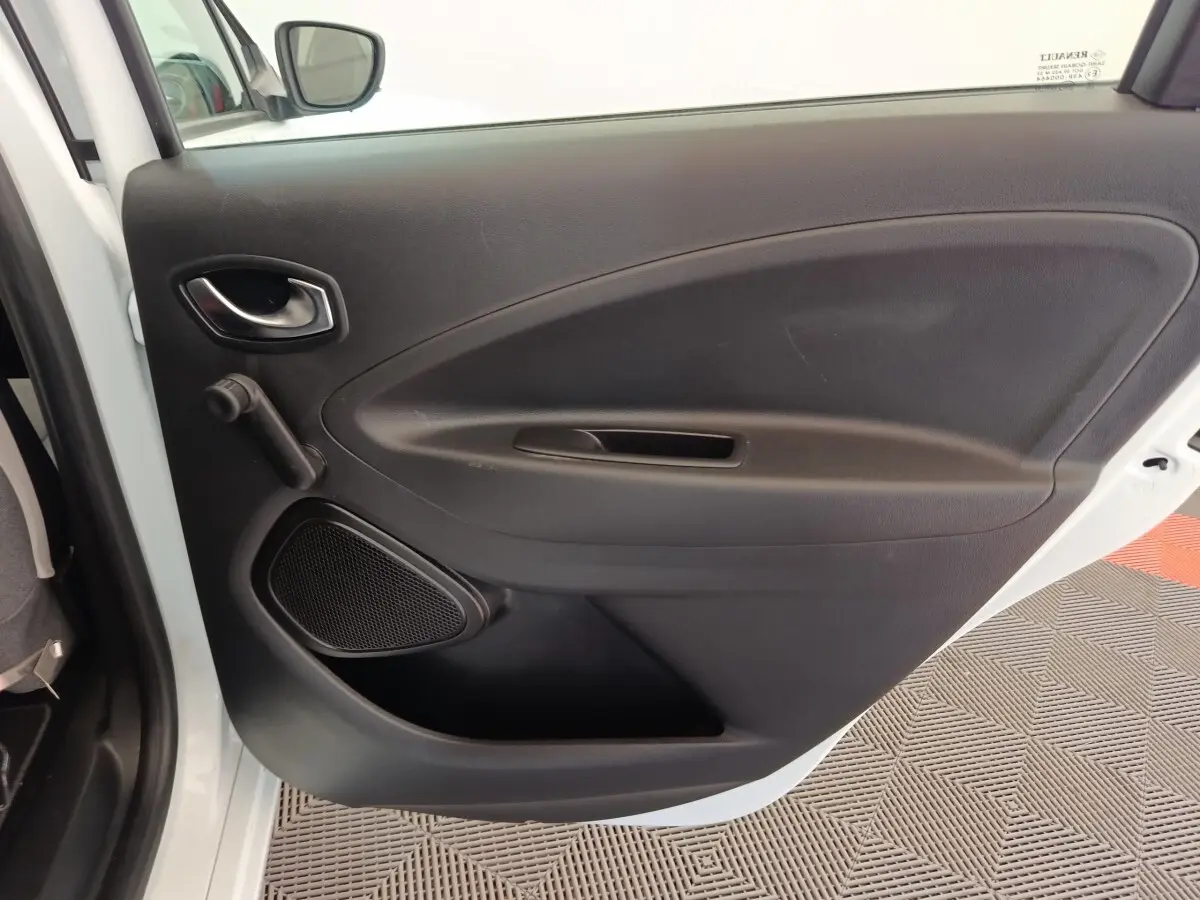 Vue intérieure de la porte arrière gauche noire de la Renault ZOE blanche Zen R135, avec poignée et haut-parleur intégrés.