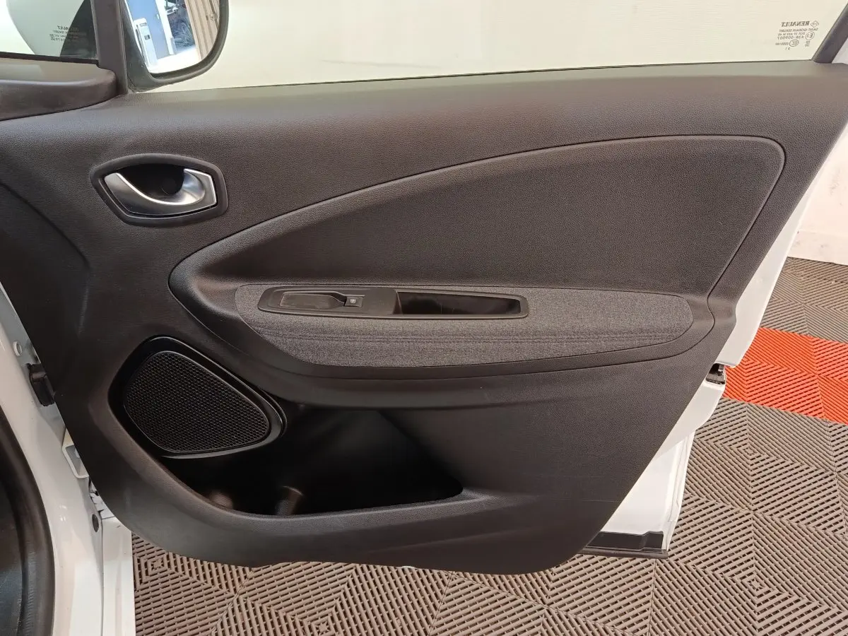 Vue intérieure de la porte avant gauche d'une Renault ZOE blanche, montrant la poignée, l'accoudoir et le haut-parleur intégré.