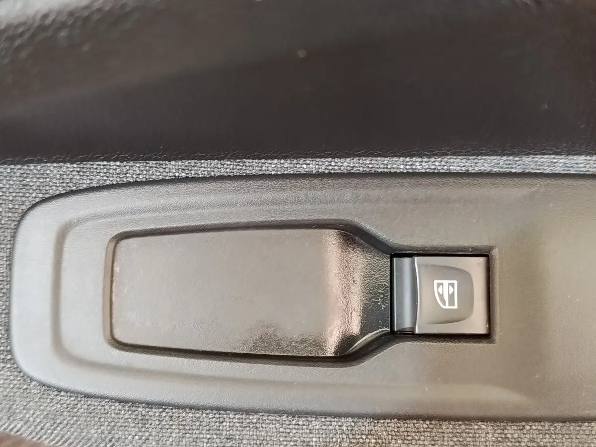 Gros plan sur le bouton de commande de lève-vitre électrique côté conducteur de la Renault ZOE blanche Zen R135 2021.