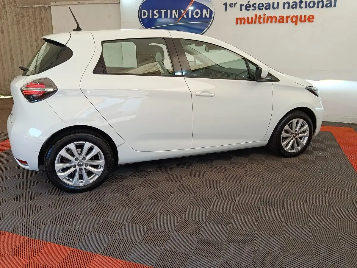 Profil droit de la Renault ZOE blanche 2021, version Zen R135, sur sol damier avec jantes alliage visibles.