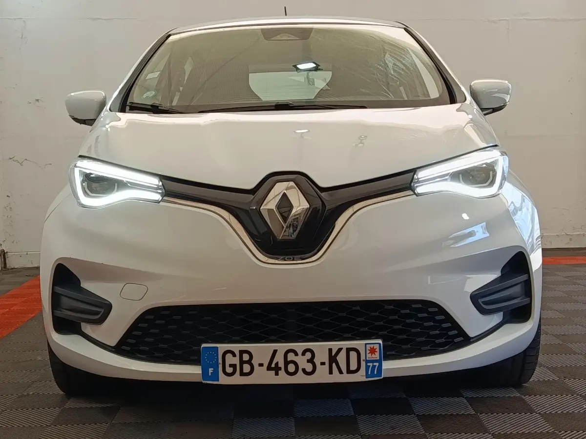 Vue avant d'une Renault ZOE Zen R135 blanche de 2021, avec phares LED allumés et calandre noire distinctive.