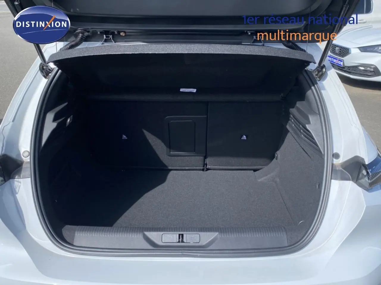 Coffre ouvert vu de l'arrière d'une Peugeot 308 Hybrid 145ch GT blanc Okenite, montrant un espace de chargement vide.