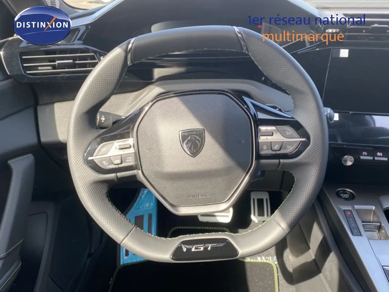 Vue rapprochée du volant cuir perforé noir avec logo Peugeot et badge GT du tableau de bord d’une 308 Hybrid 2026.