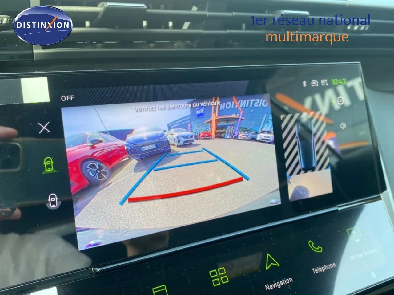 Écran tactile intérieur de Peugeot 308 Hybrid blanc montrant la caméra de recul avec vue arrière et voitures en stationnement.
