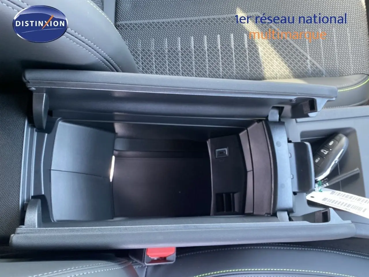 Vue plongeante sur le rangement central ouvert de la Peugeot 308 Hybrid 145ch GT, intérieur tissu noir avec surpiqûres vertes.
