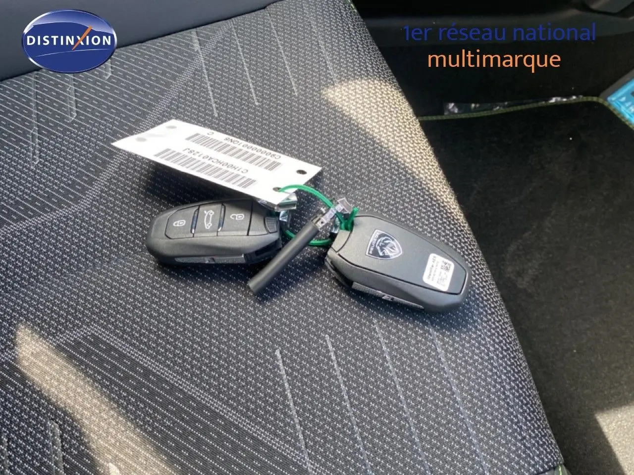Gros plan sur les clés de la Peugeot 308 Hybrid 145ch posées sur un siège tissu gris foncé à motifs blancs.