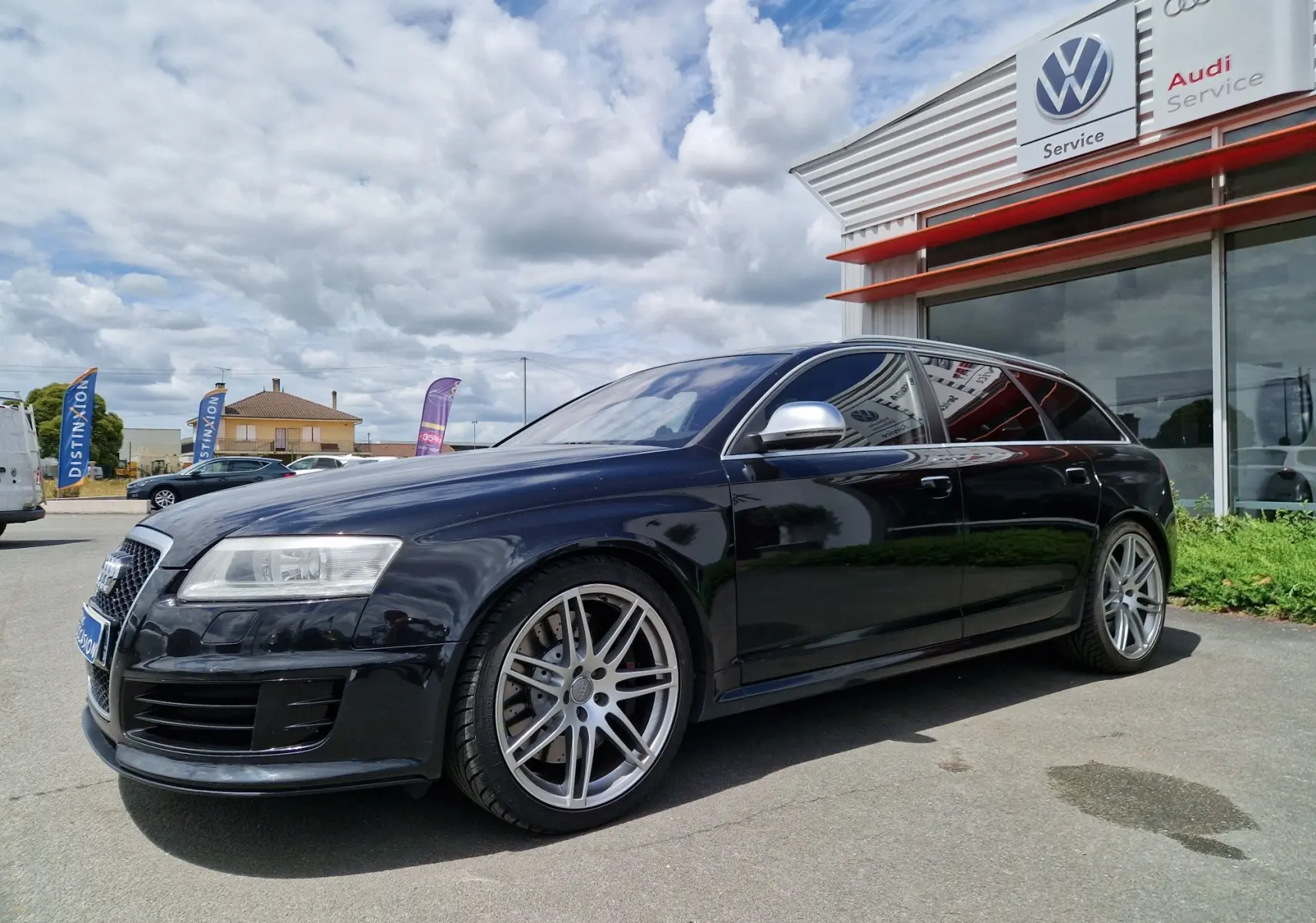 Audi RS6 Avant noire vue en 3/4 avant droit, avec jantes alliage et rétroviseurs argentés, stationnée devant un service Audi.
