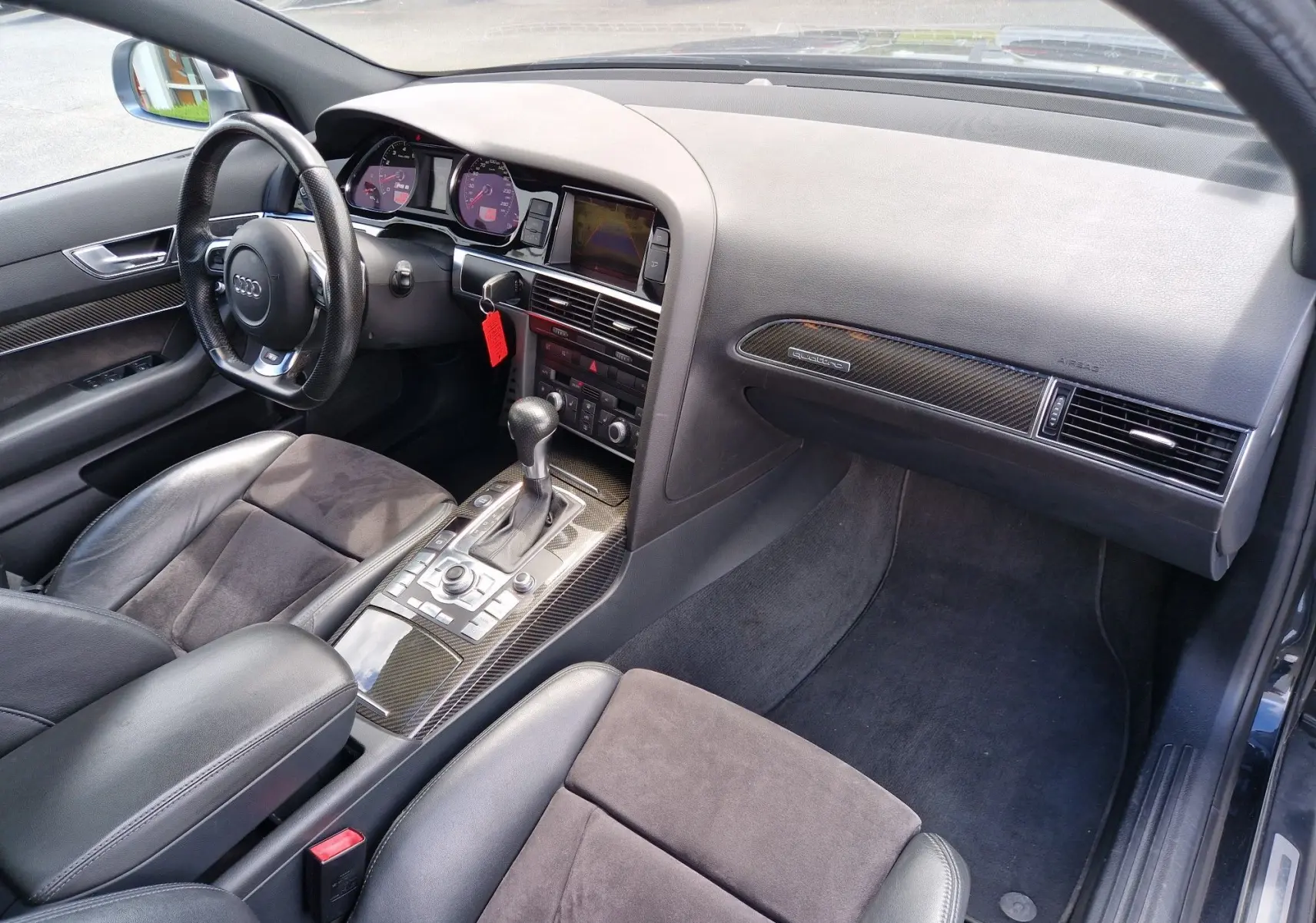 Vue intérieure côté conducteur de l'Audi RS6 Avant 2009 avec tableau de bord noir et inserts carbone, volant cuir et console centrale automatique.