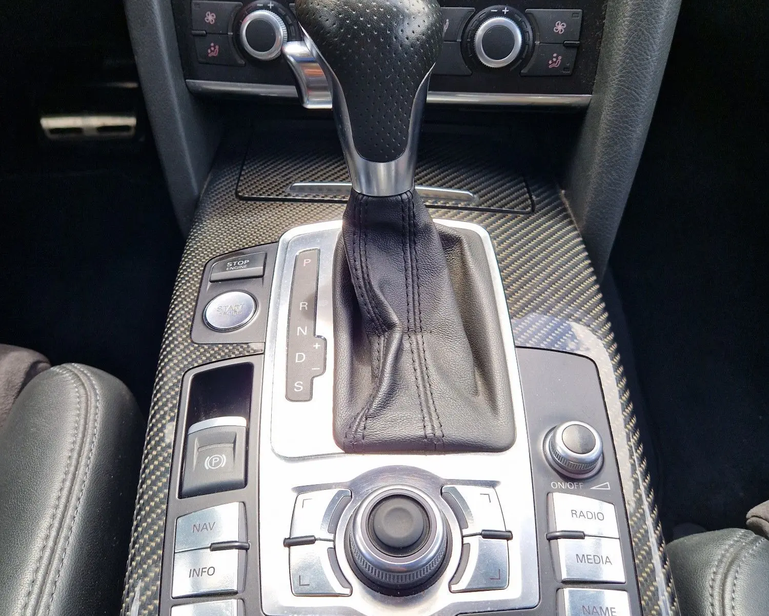 Vue rapprochée de la console centrale en carbone avec levier de vitesse automatique et commandes multimédia d'une Audi RS6 Avant noire.
