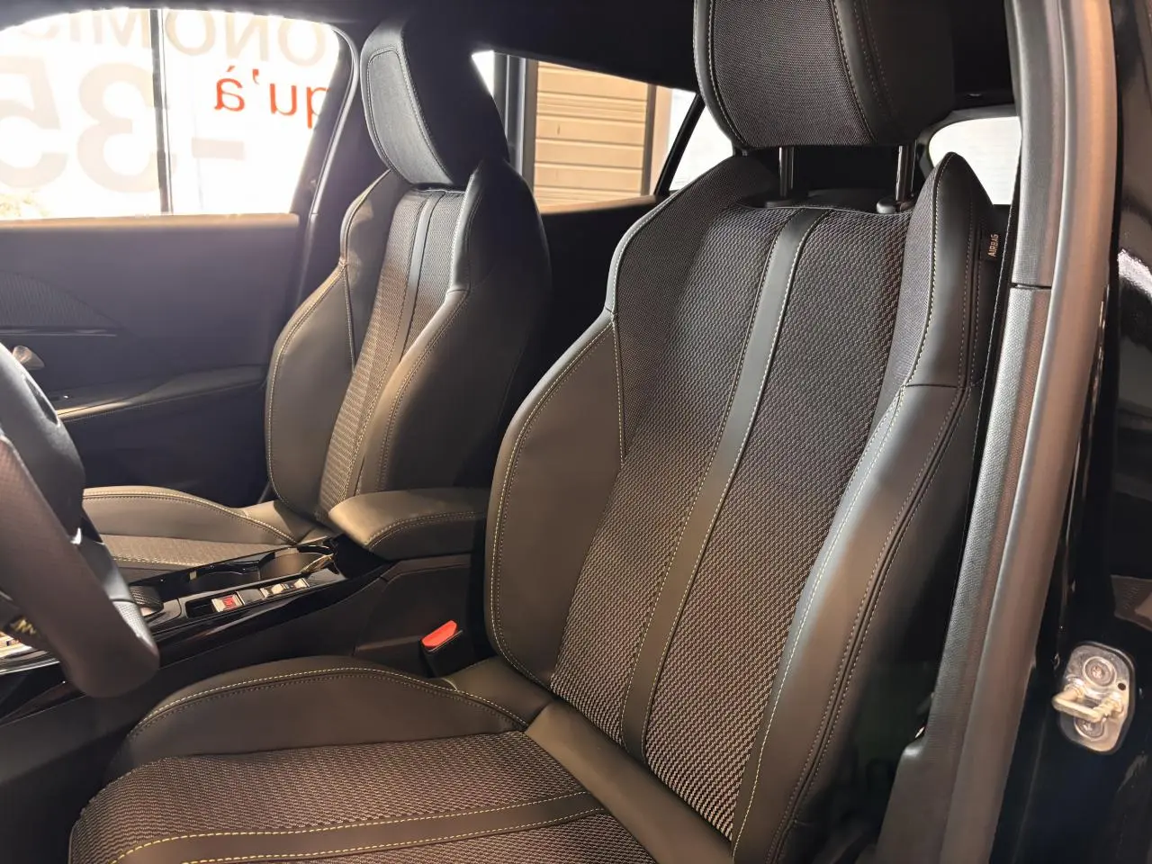 Vue intérieure côté gauche montrant les sièges avant noirs en tissu et cuir avec surpiqûres vertes du Peugeot 2008 GT 2025.