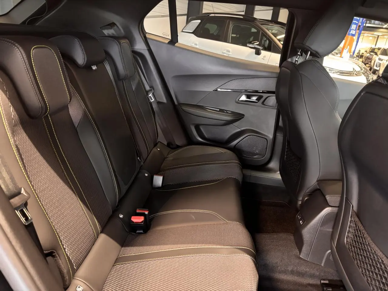 Vue intérieure arrière droite du Peugeot 2008 1.2i Hybrid GT 2025, sièges noirs avec surpiqûres vertes et panneaux de porte noirs.