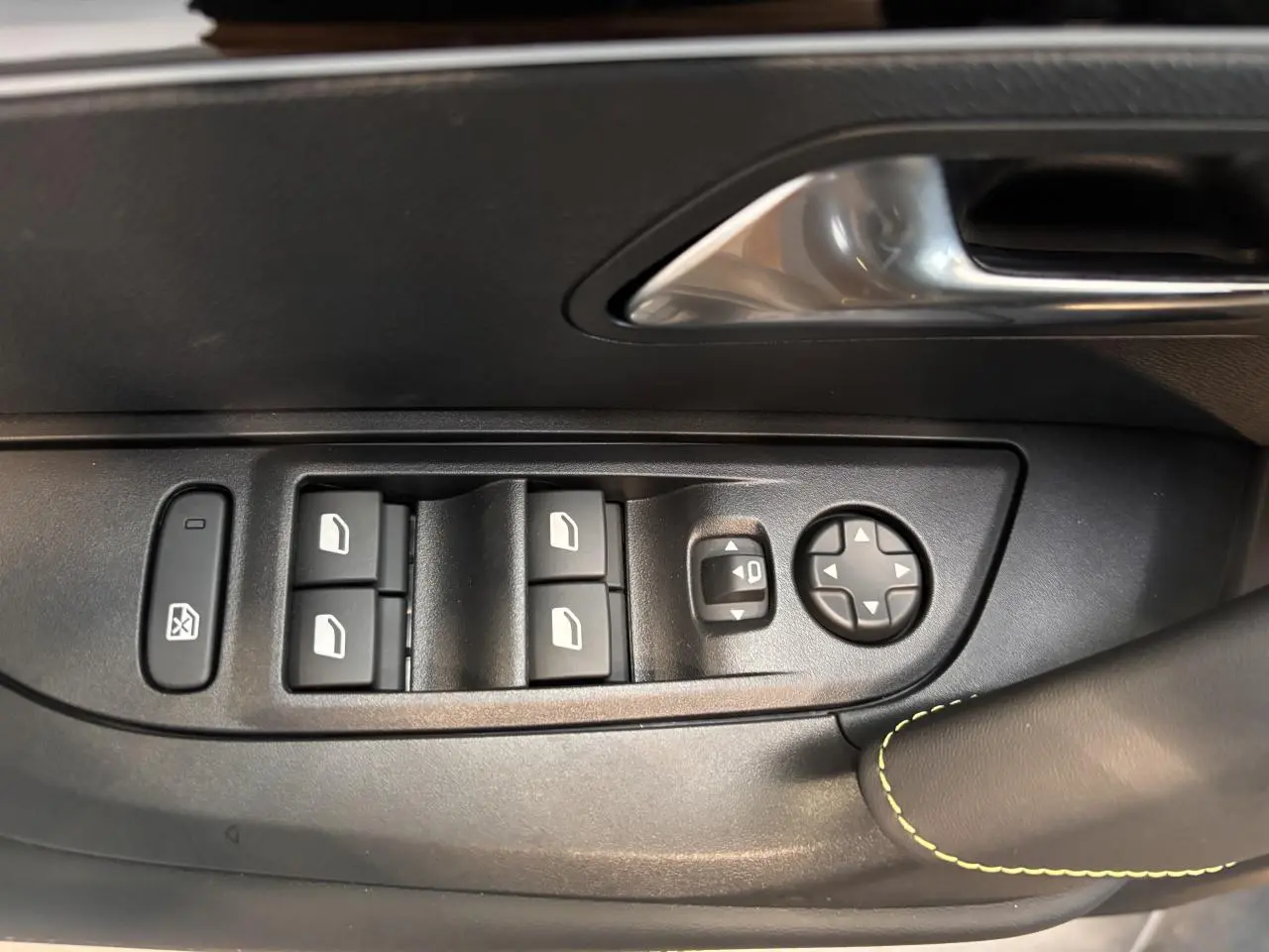 Gros plan sur les commandes de lève-vitres et rétroviseurs noirs avec surpiqûre vert Adamite sur porte avant gauche du Peugeot 2008 blanc.