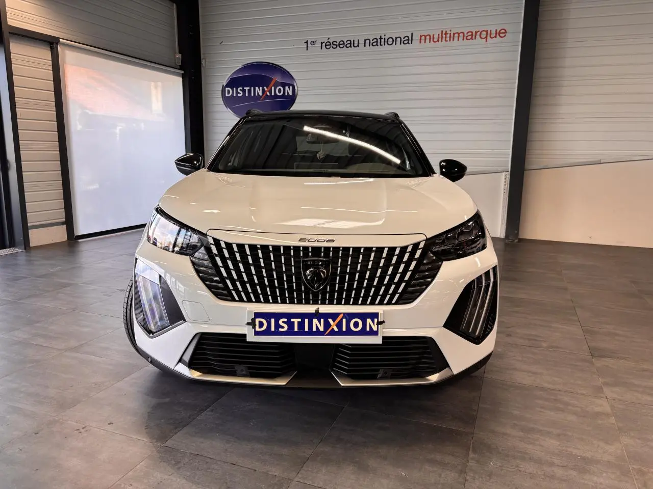 Vue frontale d'un Peugeot 2008 blanc avec calandre noire à motifs verticaux et phares LED distinctifs en intérieur showroom.