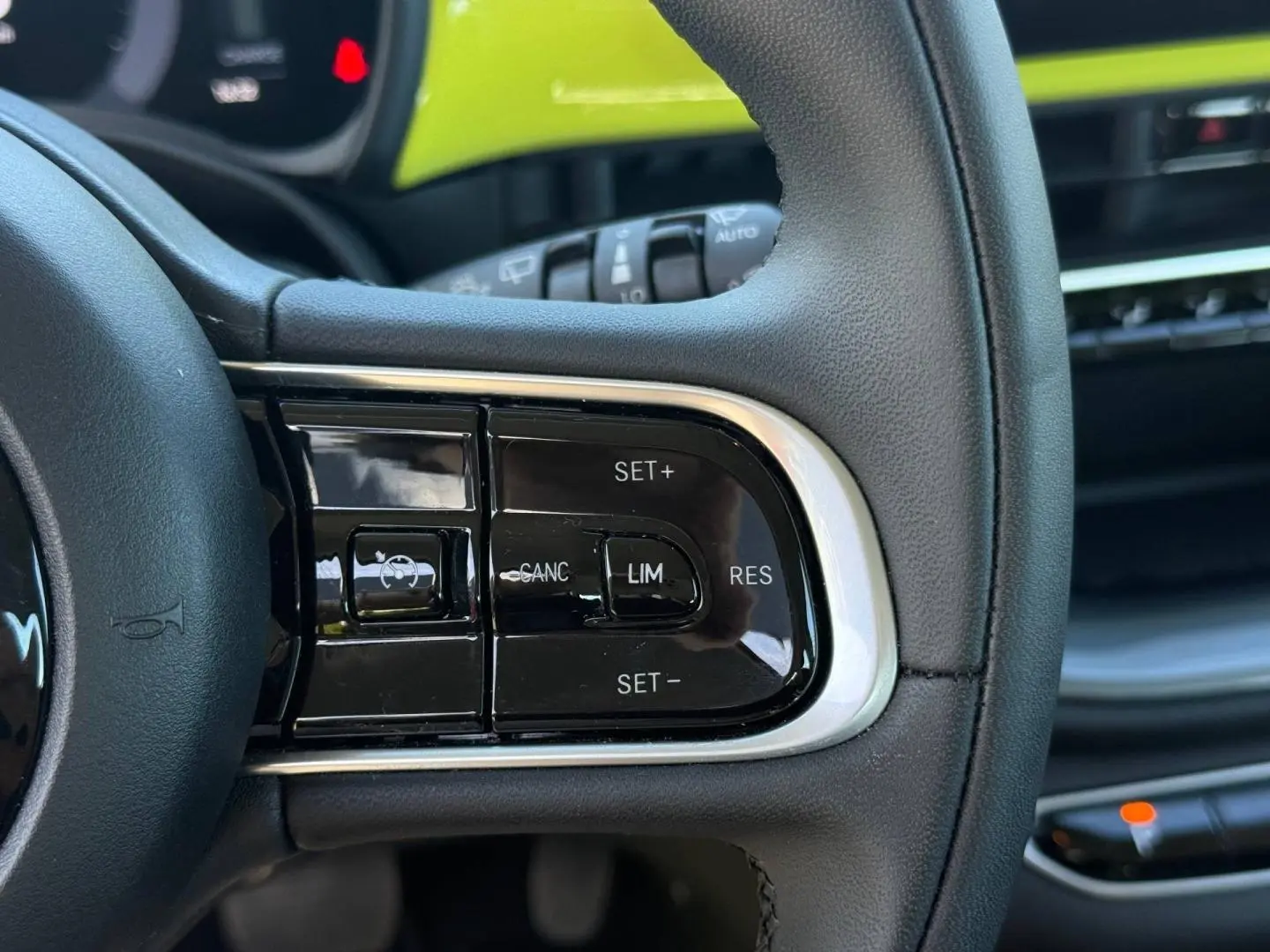 Gros plan sur les commandes du régulateur de vitesse au volant noir de la Fiat 500 électrique jaune MY24.