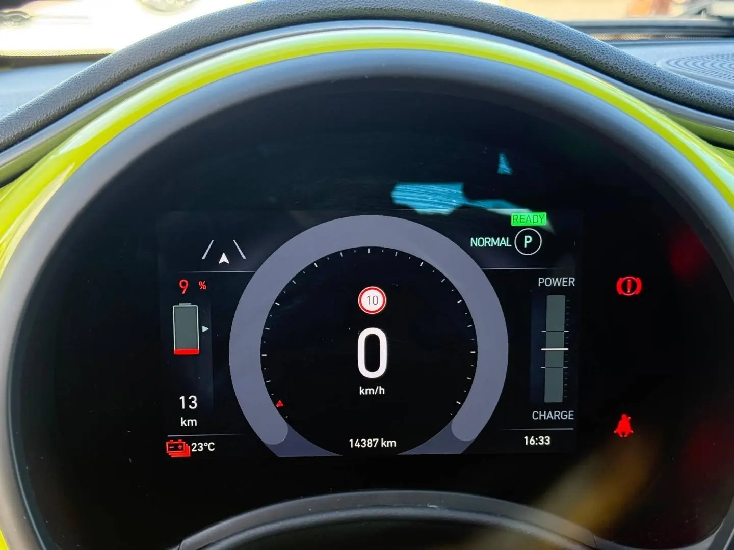 Vue rapprochée du tableau de bord numérique d'une Fiat 500 électrique jaune, affichant la vitesse à 0 km/h.