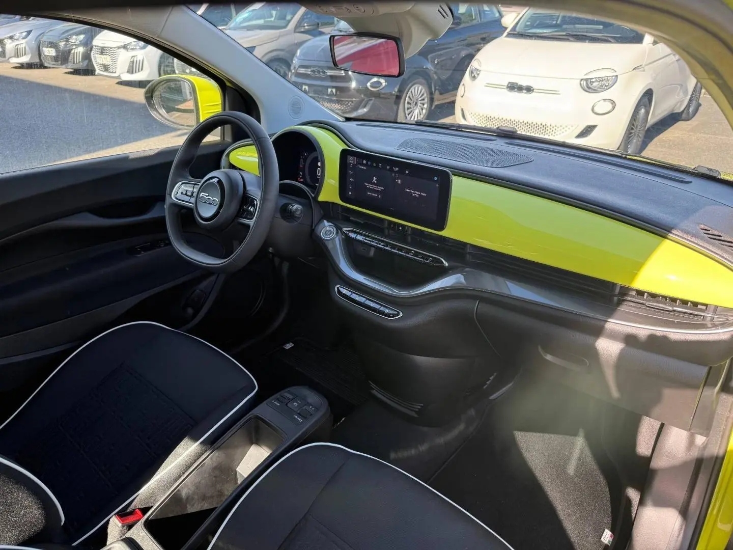 Vue intérieure côté conducteur de la Fiat 500 électrique jaune avec tableau de bord et écran tactile central.