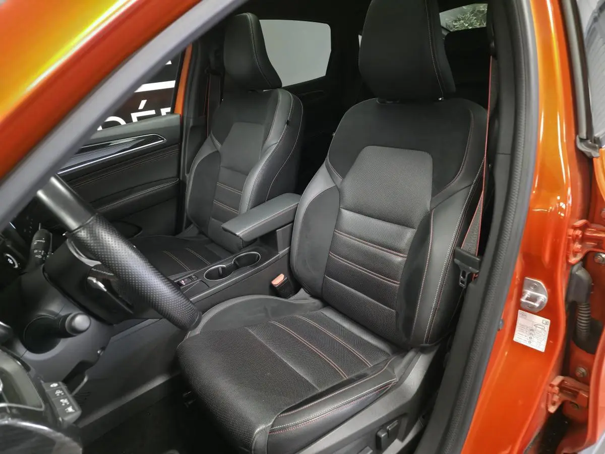 Vue intérieure côté conducteur du Renault Arkana orange, sièges sport cuir/suédine noirs avec surpiqûres rouges.
