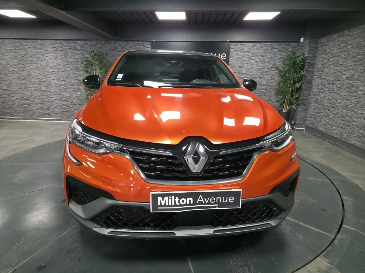 Vue frontale d'un Renault Arkana 2024 orange Valencia avec calandre noir brillant et badge R.S. Line visible.
