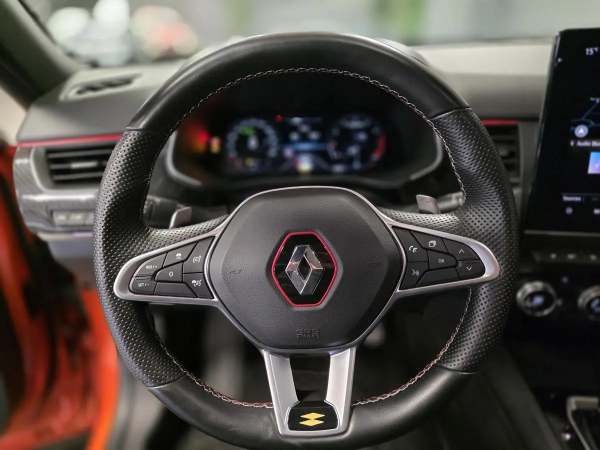 Volant sport en cuir perforé avec surpiqûres rouges et logo Renault au centre d'un Renault Arkana orange Valencia 2024.