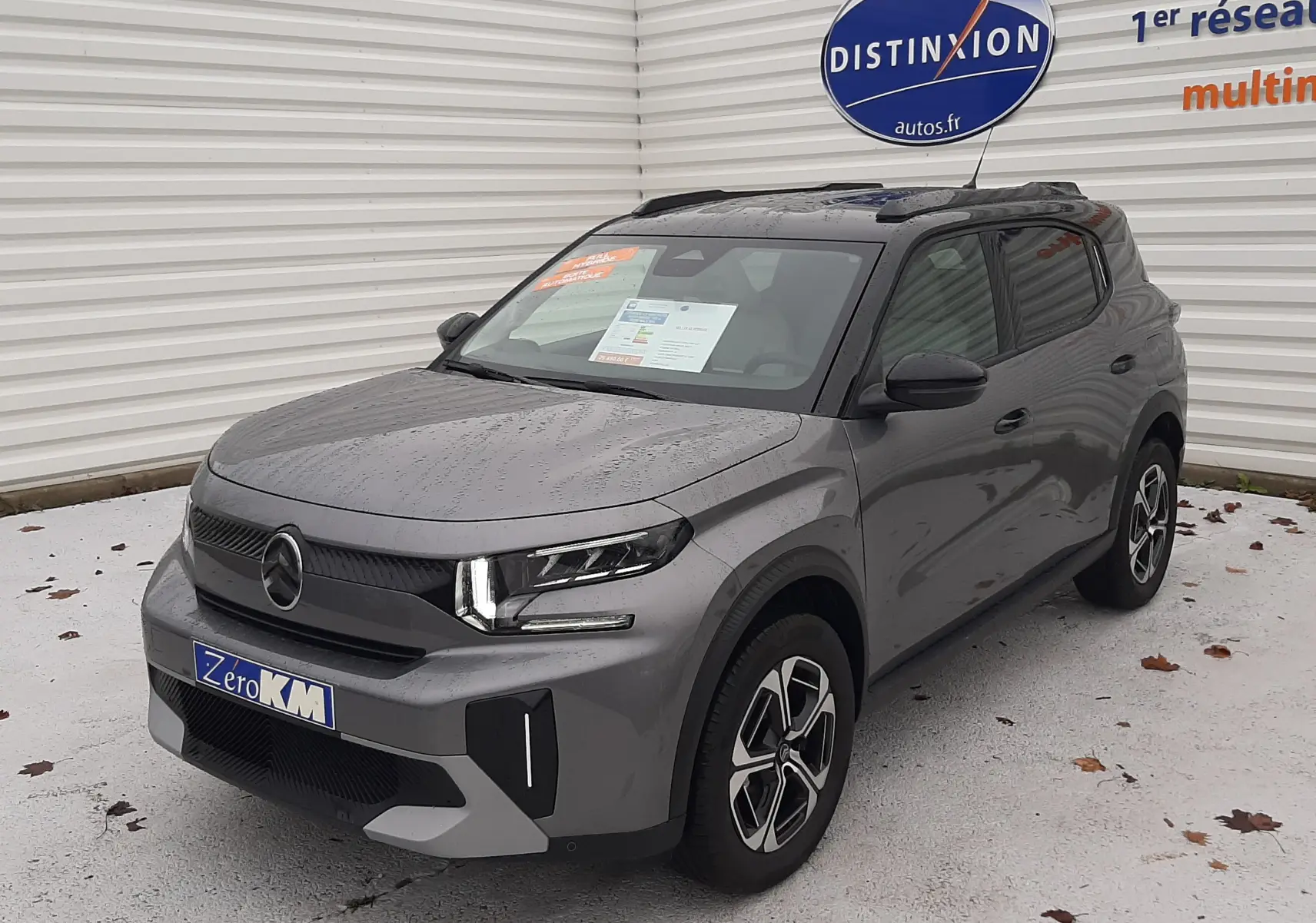 Vue 3/4 avant d'un Citroën C3 Aircross 2025 gris Mercury avec toit noir et jantes biton, stationné devant un mur blanc.