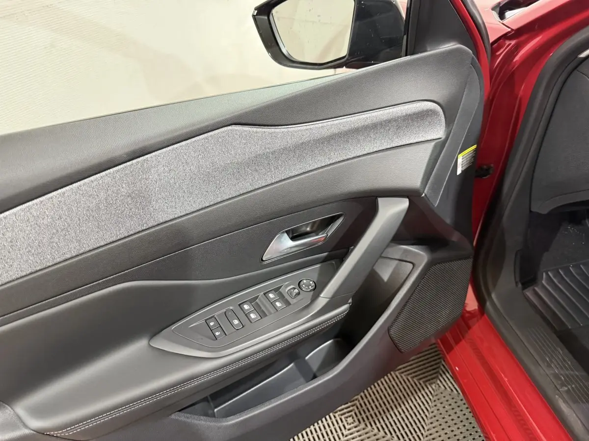 Vue intérieure côté gauche de la porte avant rouge de la Peugeot 308 BlueHDi 130 AUTO8 ALLURE avec commandes électriques.