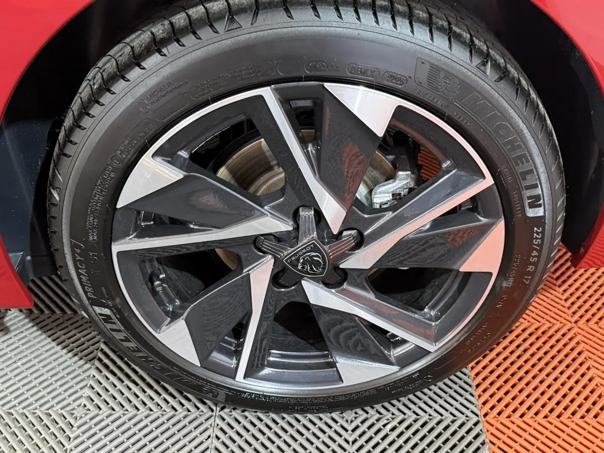 Gros plan sur la jante avant droite en alliage bicolore du Peugeot 308 rouge, avec logo lion central visible.