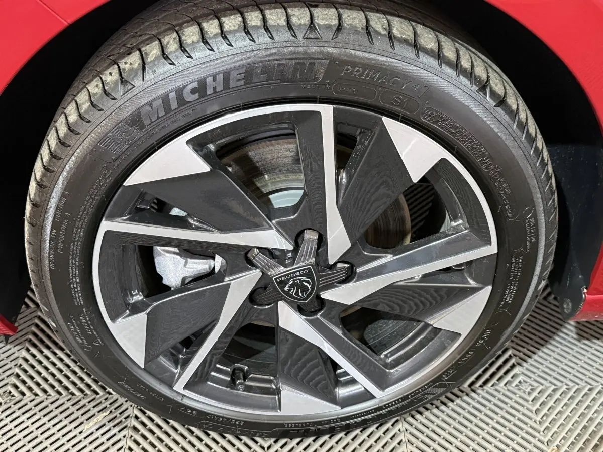 Gros plan sur la roue avant gauche d’une Peugeot 308 rouge 2025 avec jante alliage bicolore et pneu Michelin.