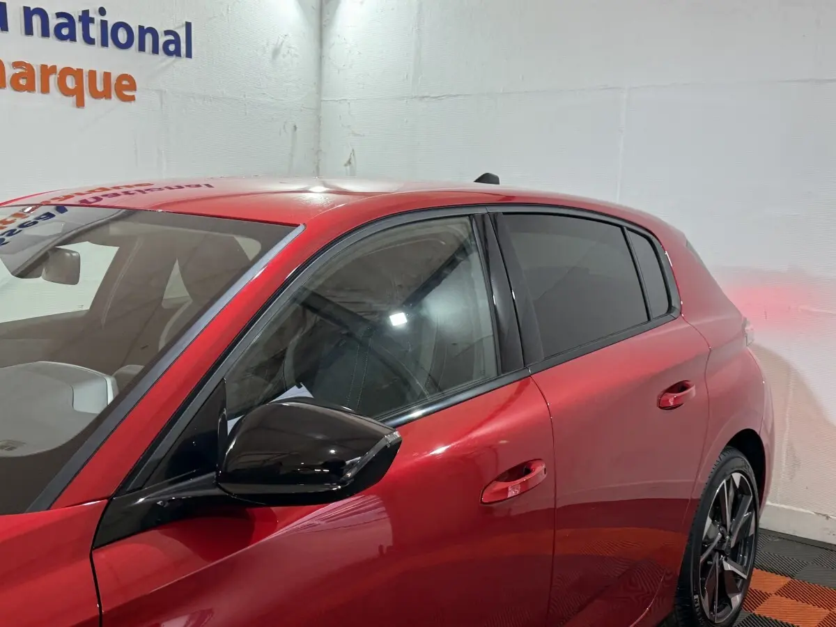 Vue latérale gauche d’une Peugeot 308 rouge 2025 avec rétroviseur noir et vitres teintées.
