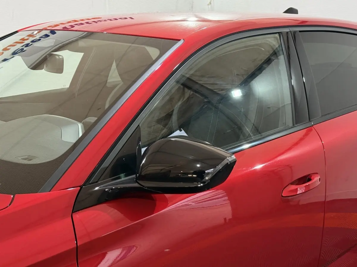 Vue rapprochée du côté avant gauche de la Peugeot 308 rouge avec rétroviseur noir brillant et poignée de porte intégrée.