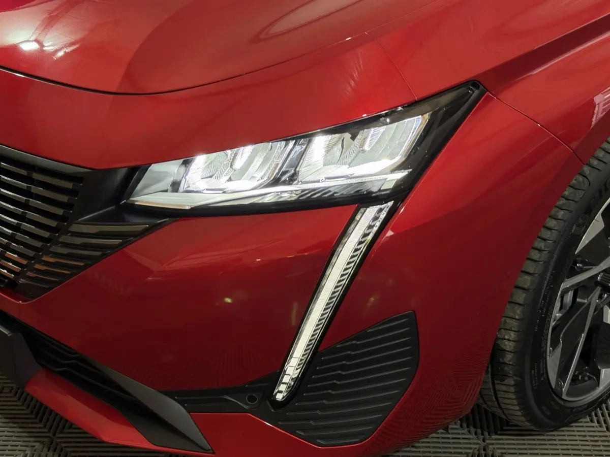 Gros plan sur l’avant droit rouge de la Peugeot 308 2025, mettant en valeur le phare LED et la calandre noire.