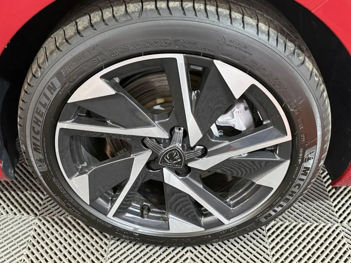 Gros plan sur la jante alliage bicolore et pneu Michelin d’une Peugeot 308 rouge, côté avant droit.