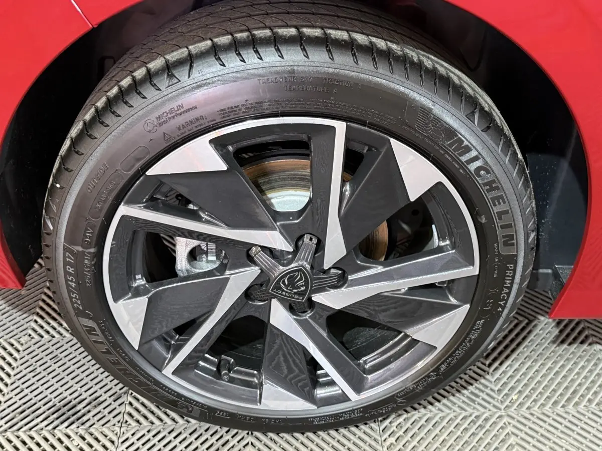 Gros plan sur la roue avant gauche d’une Peugeot 308 rouge, avec jante alliage bicolore et pneu Michelin.