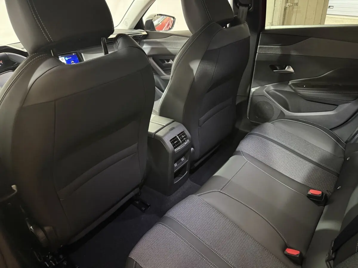 Vue intérieure arrière montrant les sièges noirs et la console centrale d'une Peugeot 308 BlueHDi 130 AUTO8 Allure rouge.