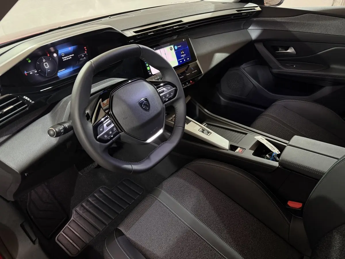 Intérieur de la Peugeot 308 2025 vue côté conducteur, volant cuir, tableau de bord numérique et écran tactile central.