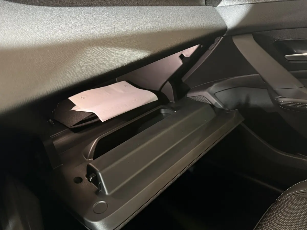 Intérieur de la Peugeot 308 2025, vue sur la boîte à gants ouverte côté passager avec documents visibles.