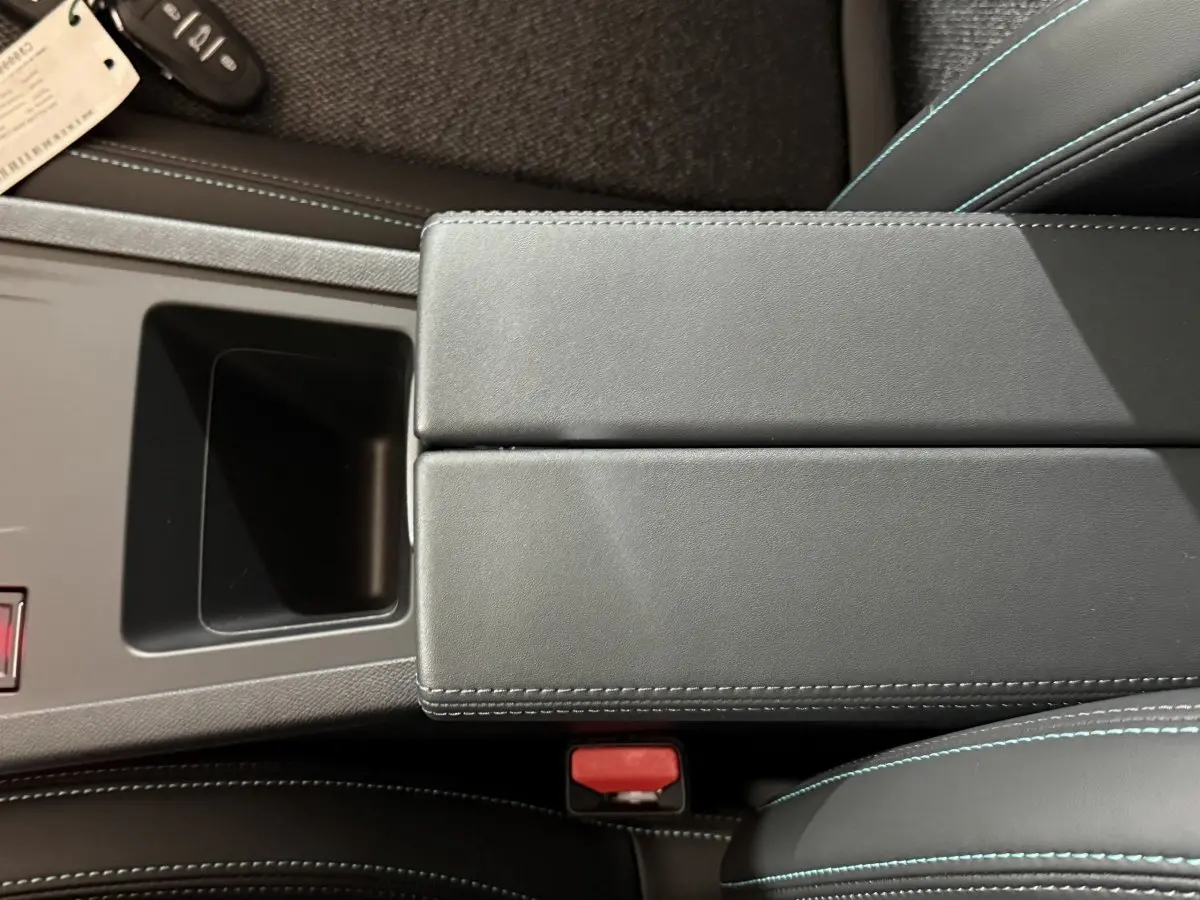 Vue rapprochée de l'accoudoir central noir et des sièges en cuir avec surpiqûres bleues dans une Peugeot 308 rouge.