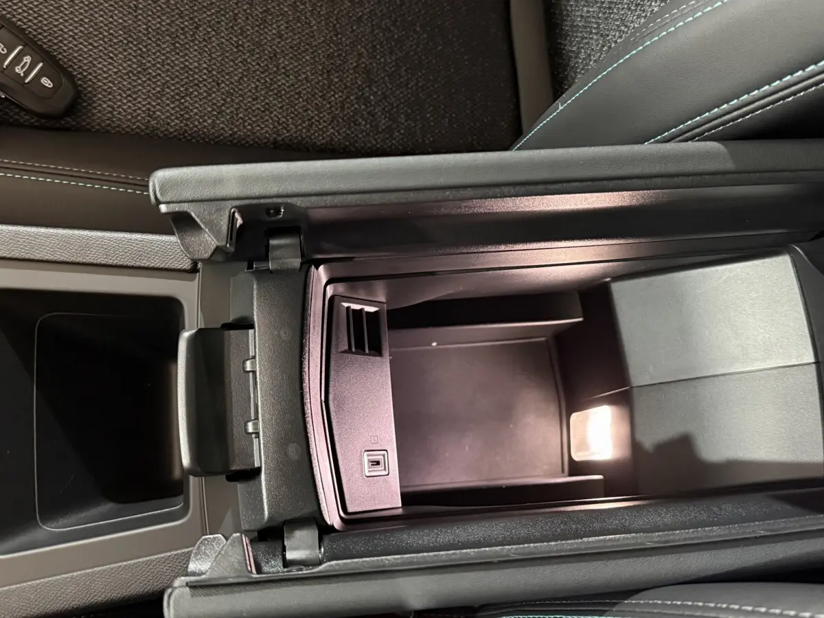 Vue intérieure en plongée du rangement central ouvert de la Peugeot 308 rouge, soulignant les finitions en cuir noir et coutures bleues.