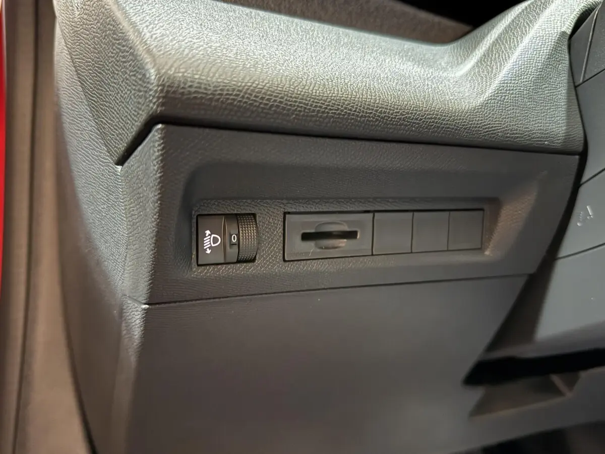 Détail intérieur côté gauche du tableau de bord noir de la Peugeot 308 rouge, avec commande réglage phares.