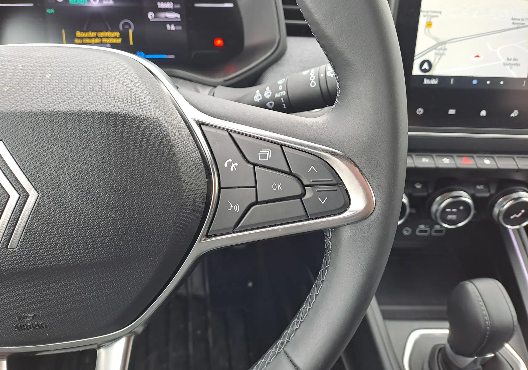 Gros plan sur le volant côté droit de la Renault Clio V 2025, avec commandes intégrées et tableau de bord numérique en arrière-plan.