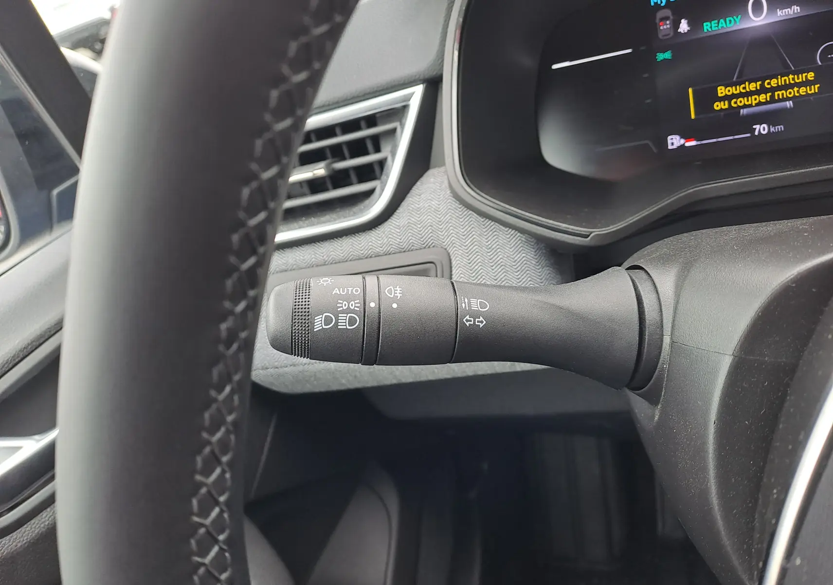 Gros plan sur la commande des phares à gauche du volant dans l’habitacle noir de la Renault Clio V hybride 2025.